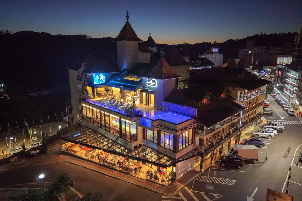 Vista aérea noturna do Hotel Rouxinol iluminado, com o estacionamento em frente, em Piratuba (SC)