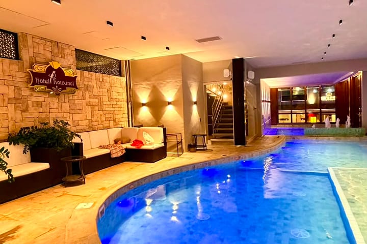 Piscina interna aquecida do Hotel Rouxinol, com sofás e iluminação ambiente